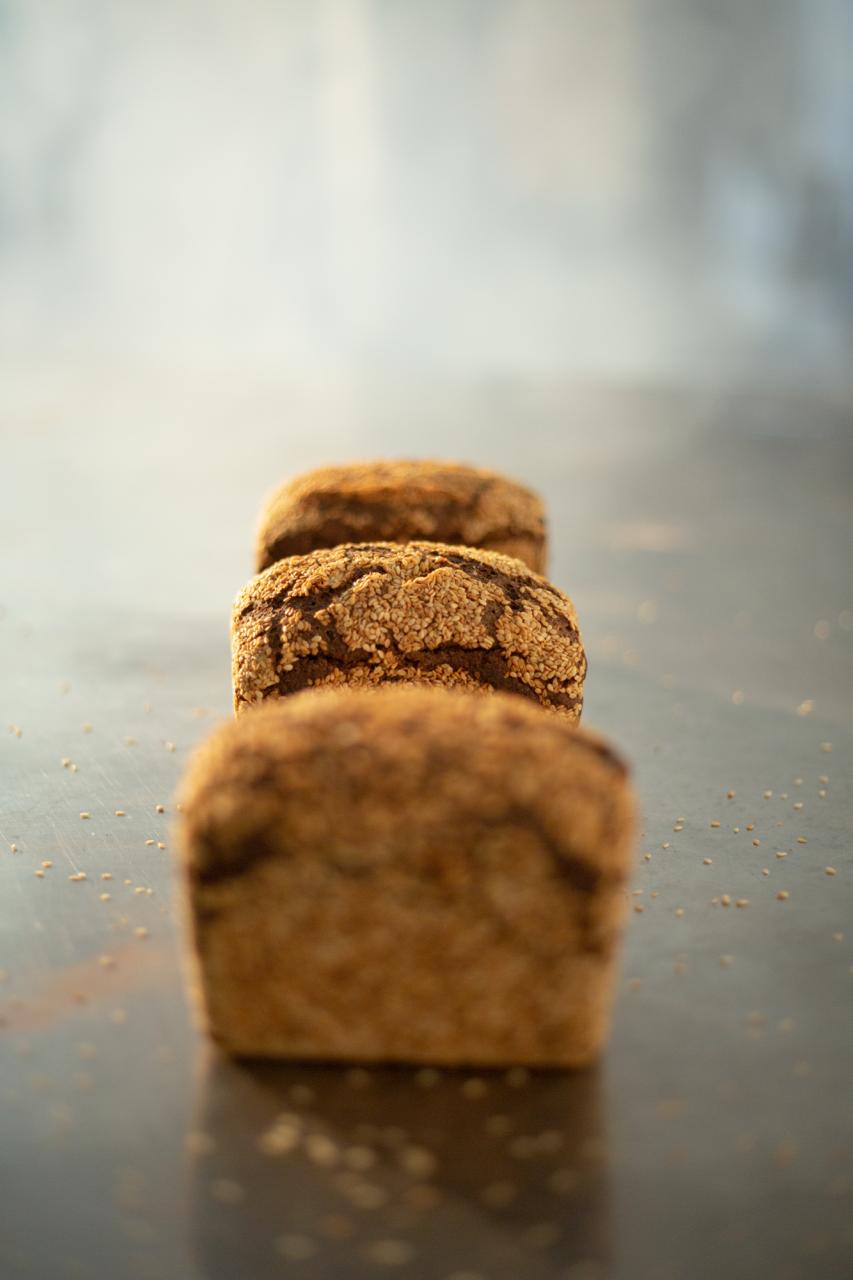 Artisan gluten-free bread loaves with sesame seeds on dark surface